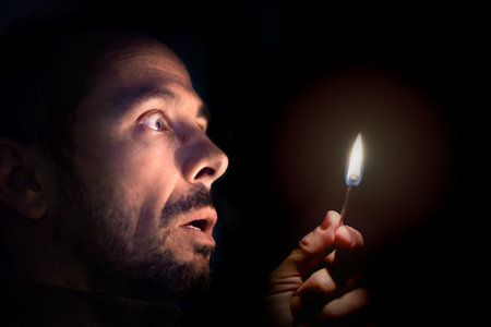 Worried man with a match in the dark. Blackout concept.の写真素材