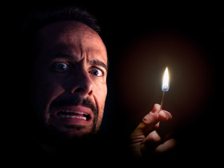 Worried man looking at the camera with a match in the dark. Blackout concept.の写真素材