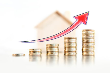 Stack of coins with an arrow and a wooden house in the background. Concept of purchase, rent and mortgage expense.の写真素材