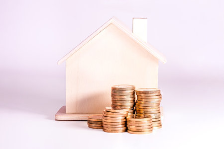 Pile of coins with a wooden house in the background. Concept of purchase expense, rent and mortgage.の写真素材