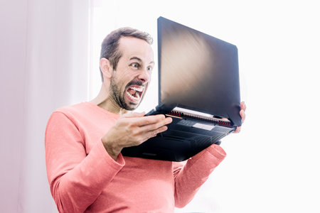 Angry man working at home with his laptop in his handsの写真素材