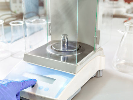 A operators hand is holding steel calibration weight to place on the analytical balance. Concept of quality control in a laboratory.の写真素材