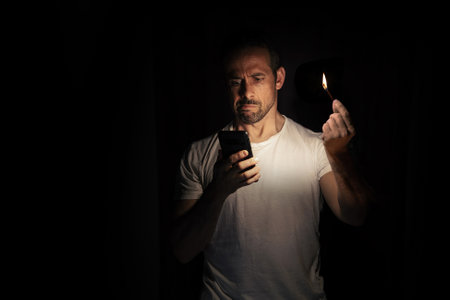 Man looking at his cell phone with a match in the dark. Blackout concept. Selective focus.の写真素材