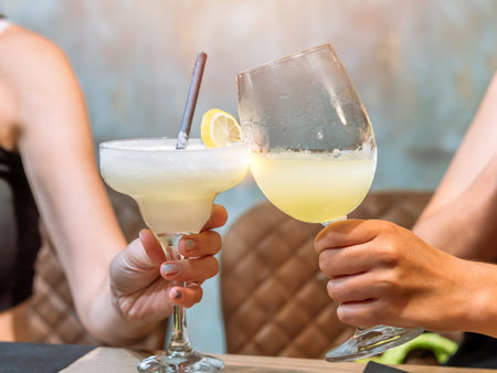 Two people holding cocktails, one margarita and one in a wine glass, garnished with lemon.の写真素材
