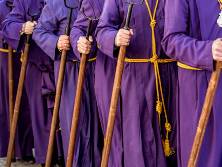 People in purple robes and yellow belts, holding wooden staffs during a procession. Selective Focus.