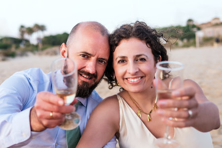 A couple toasts with wine glasses on a beach at sunset, celebrating a special moment.の写真素材