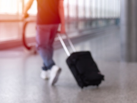 Unfocused photo of unrecognizable man walking with suitcase in airport terminalの写真素材