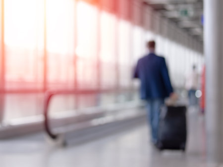 Unfocused photo of unrecognizable man walking with suitcase in airport terminalの写真素材