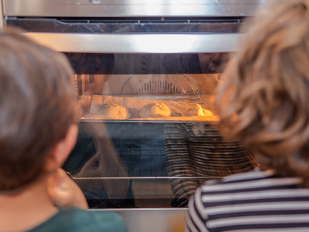 Two children watching baked goods rise in ovenの写真素材