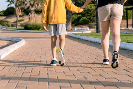 Woman walking hand in hand with her son through a green park pathway
