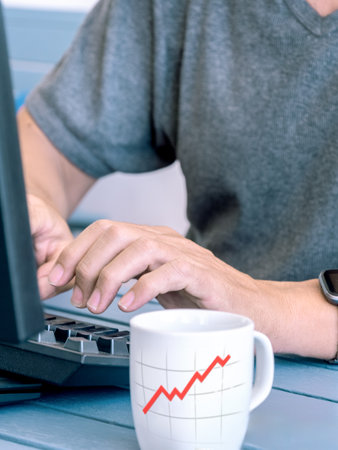 Man working on laptop with rising graph mug