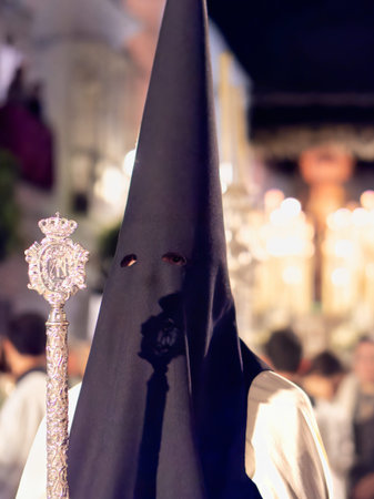 Nazareno wearing black hood and white robe holding a silver processional staff at nightのeditorial素材