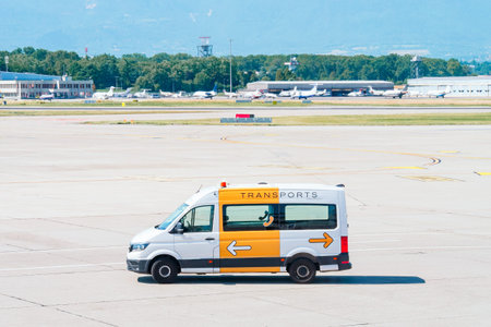 White airport transport van driving on a sunny tarmac at a busy airfield