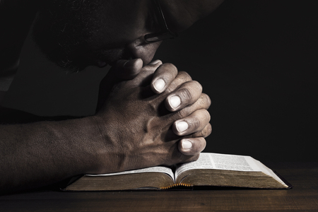 Man praying to God on a Bible in a dark place.