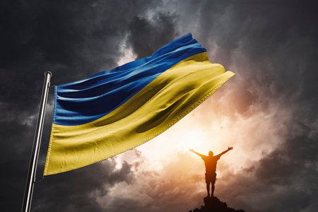 Ukraine flag in a sunset with dramatic storm clouds and a Ukrainian men raising his hands in victory.の写真素材