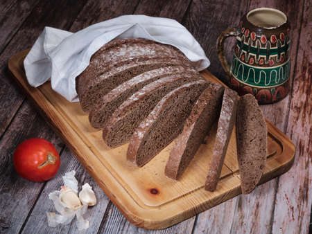 Sliced rye bread on cutting board , tomato and garlicの写真素材