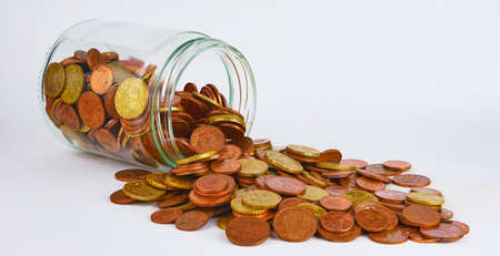 euro coins in a glass jar against a white backgroundの写真素材