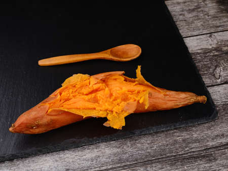 Baked sweet potato on dark stone. Wood table and spoonの写真素材