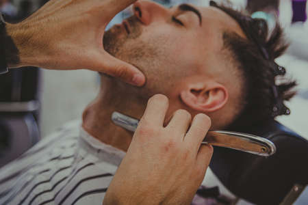 detail of a young man with tattooed arms cuts a man's hair in a barber shopの写真素材