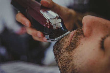 detail of a young man with tattooed arms cuts a man's hair in a barber shopの写真素材