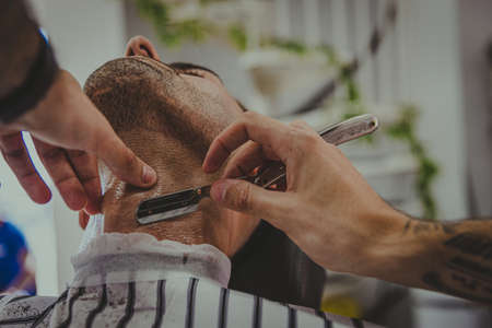 detail of a young man with tattooed arms cuts a man's hair in a barber shopの写真素材