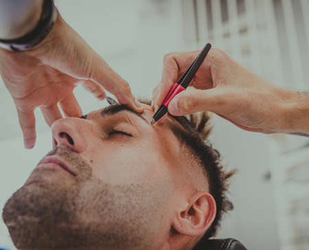 detail of a young man with tattooed arms cuts a man's hair in a barber shopの写真素材