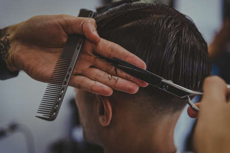 detail of a young man with tattooed arms cuts a man's hair in a barber shopの写真素材