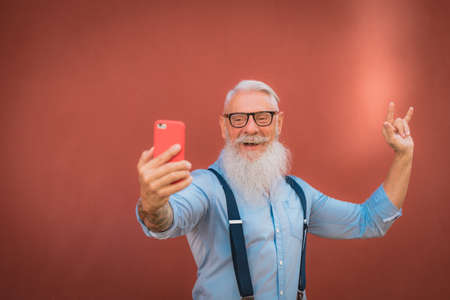 an older man in hipster clothes and glasses and a long white beard walks around talking on the phone focus on headの写真素材