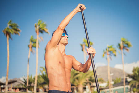young man prepares to paddle surf on a beach