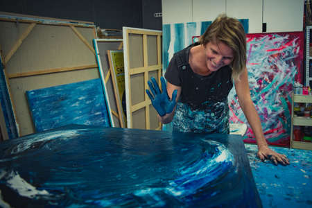 Young woman paints an abstract picture with her hands and spatula on a work table in her interior...