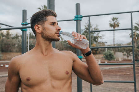 young man exercises with face mask outdoors and drink waterの写真素材