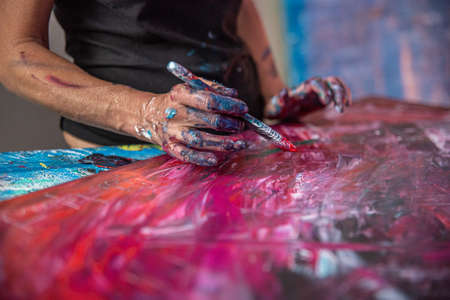 Young woman paints an abstract picture with her hands in her interior studio, focus on hand