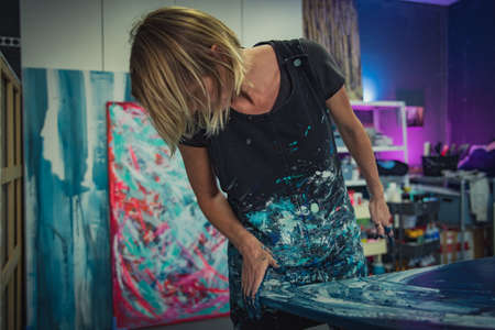 Young woman paints an abstract picture with her hands and spatula on a work table in her interior studio. Focus on headの写真素材