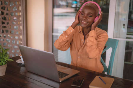 black adult woman listens to music looks happy while working on her computer in a coffee shop focus...