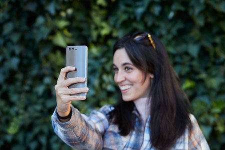 Smiling girl taking a selfie with a smartphone on an ivy backgroundの写真素材