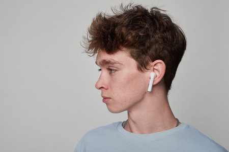 Side view of a young man putting on earphones in a photo studio with a gray backgroundの写真素材