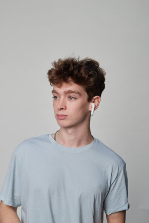 Side view of a young man putting on earphones in a photo studio with a gray backgroundの写真素材