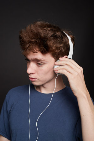 Side view of a young man putting on headphones in a photo studio with a gray backgroundの写真素材