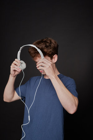 Side view of a young man putting on headphones in a photo studio with a gray background