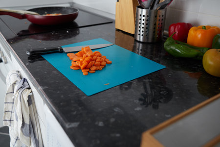 Carrot cut on a blue board, while the vegetables are poached in the frying panの写真素材