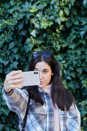 Smiling girl taking a selfie with a smartphone on an ivy backgroundの写真素材