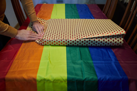 Anonymous person folding a gift wrap on a table with a tablecloth with the colors of the lgtbi flagの写真素材