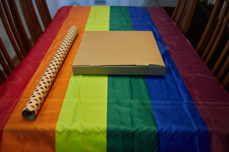 Cardboard box with hearts wrapping paper on a table with a tablecloth with the lgtbi flagの写真素材