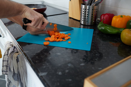 Anonymous person cutting carrots on a blue board, while the vegetables are poached in the panの写真素材