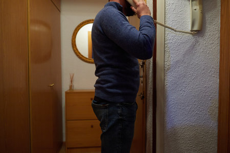 Side view of an unrecognizable man in casual clothes standing near the door and answering the phoneの写真素材