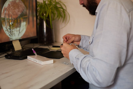 Anonymous man taking a swab out of the wrapper for a rapid coronavirus test in a room with a computerの写真素材