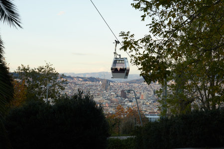 Close up of gray cable car descending from high mountain. Behind the cable car you can see a big city with mountains in the backgroundの写真素材