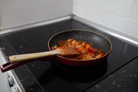 Frying pan with cooked vegetables and a wooden paddle on an induction ceramic hobの写真素材