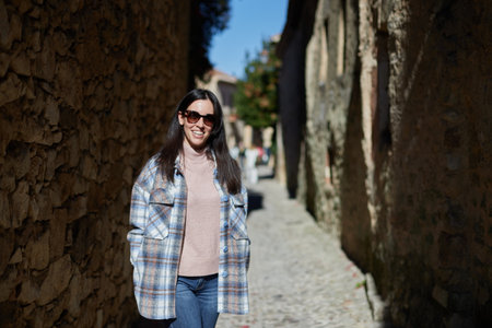 Smiling girl with sunglasses and coat strolling through the sunny townの写真素材