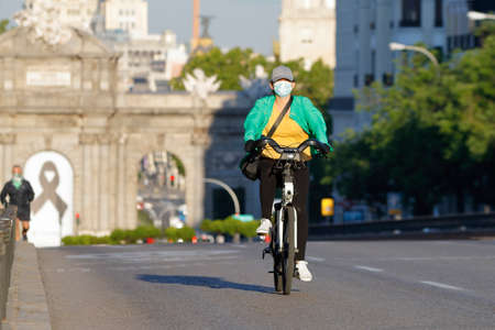 Madrid, Spain - 22 May 2020: Woman goes to work on a public bicycle with a mask during the...